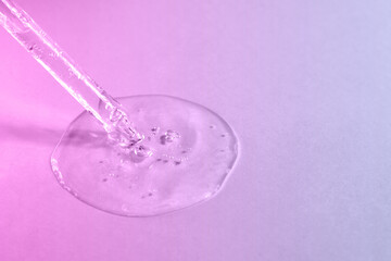 Facial serum with bubbles pouring from glass pipette on pink and purple background closeup. Trendy neon gradient. Beauty and spa concept. Cosmetic product with hyaluronic acid. Copy space, front view.