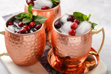 Traditional american alcoholic beverage moscow mule in copper mugs with cranberry and mint on white marble board - non-alcoholic cocktail version