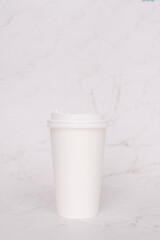 Take-out coffee with a white lid on top of the marble background.