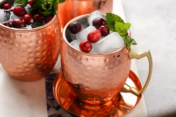 Traditional american alcoholic beverage moscow mule in copper mugs with cranberry and mint on white marble board - non-alcoholic cocktail version