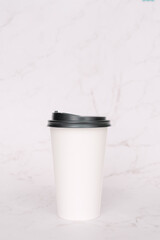 Take-out coffee with a black lid on top of the marble background.