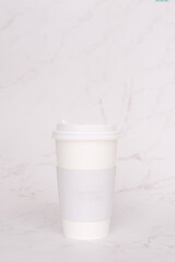 Take-out coffee with a white lid on top of the marble background.