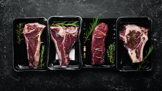 Set of beef steak in vacuum packing. Market. Top view. Flat lay top view on black stone cutting table.
