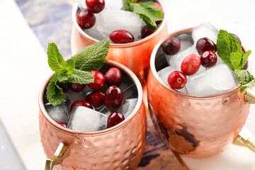 Traditional american alcoholic beverage moscow mule in copper mugs with cranberry and mint on white marble board - non-alcoholic cocktail version