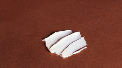Fototapeta na wymiar Smear of white face cream on brown background. Cosmetic product texture