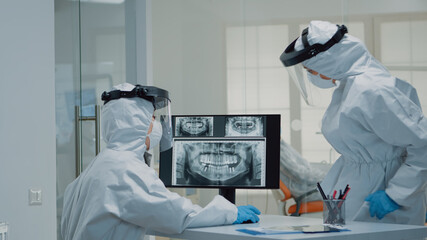 Medical dentistry staff with ppe suits using modern technology while consulting patient with oral care issues. Stomatologist and dental nurse looking at teeth animation model for implant