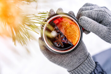Mulled wine in the hands of a girl during a snowfall in the forest. Winter hot drinks with aromatic...