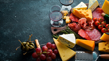 Italian appetizers. Cheese, wine, salami and prosciutto on a black stone background. Top view. Free...