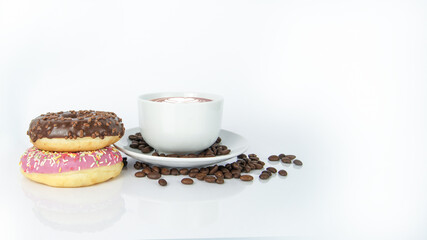 Aromatic coffee latte with leaf on the top in white cup on plate covered by brown seeds next to doughnuts. Chocolate and raspberry snacks on white background. Isolated objects in composition