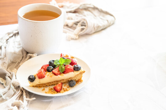 piece of strawberry and blueberry cheescake on plate and cup of tea served for breakfast at home, hotel or cafe. Dessert meal, sweet food . High quality photo