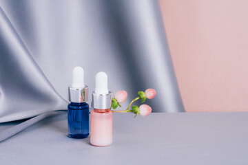 Glass bottles with hypericum on a shiny pink and gray fabric background. Serum or essential aroma oil. Health and medicine concept. Front view, copy space