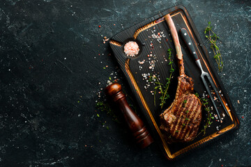 Bone steak. Tomahawk steak on a black wooden background. Top view. Free space for text.