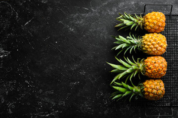 Sweet baby pineapple on a black stone background. Tropical fruits. Top view. Free space for text.