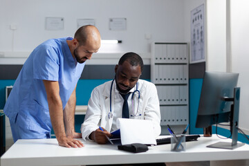African american doctor analyzing pharmaceutical documents discussing medicine prescription working at healthcare treatment in hospital office. Therapist man nurse monitoring sickness expertise