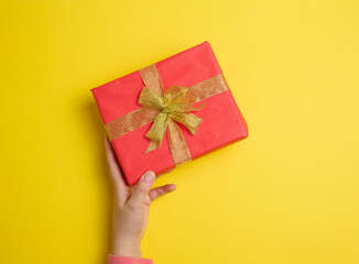 female hand holding red gift box on a yellow background, concept of congratulations