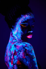 slim and beautiful sensual woman black appearance in fluorescent paint makeup, posing at camera. luminescence paint, body art, neon lights. isolated on dark background. portrait