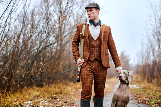 hunter in classic suit with dogs hunting bird woodcock in forest, with rifle shotgun . brutal male with trained purebred dog in rural area pace, forest. companion dog as friend. weekends outdoors