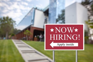 Outdoor lawn sign now hiring apply inside with a direction arrow. Employment, understaffed business