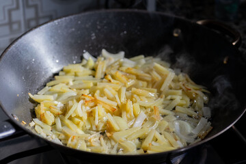 onion and friendose cut potato over vegetable oil in a black skillet