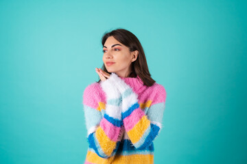 A young woman in a bright multicolored sweater on a blue background smiles cutely, holds her palms...