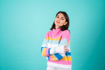 A young woman in a bright multicolored sweater on a blue background smiles cutely, looks at the...