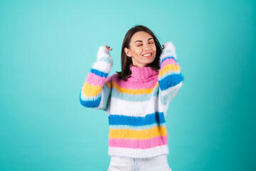 A young woman in a bright multi-colored sweater on a blue background laughs fervently, smiles,...