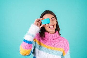 Young woman in a bright multi-colored sweater on a blue background shows a credit card, fools...