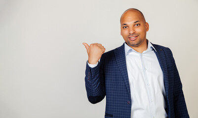Young African American man smiling positively, smiling with happy face, looking and pointing to the side with thumb up. Black man