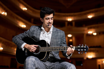 american brunette Guitar player in elegant suit performing playing guitar solo sound at concert...