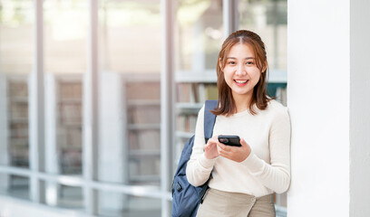 Young female university student with backpack using smartphone outdoors.