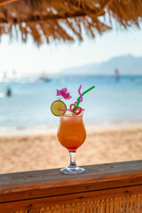 Cocktail in glass on the beach, summer drinks with blurred sea and mountains in the background