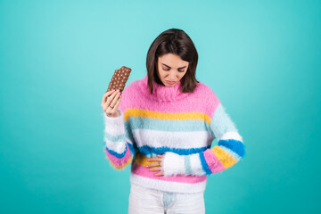 Young woman in a bright multicolored sweater on a blue background suffering from indigestion and...