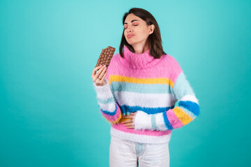 Young woman in a bright multicolored sweater on a blue background suffering from indigestion and...