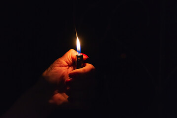 Woman hand holding a burning lighter in the dark black background.Closeup,selective focus.Copy...