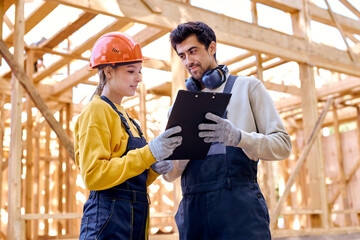 two smart architects constructors holding clipboard blueprints at construction site while...