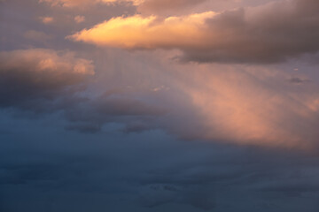 Moody sky with ray of light illuminating dark blue and bright orange clouds. clouds in a stormy sky. no people, clouds only. High contrasts in the sky