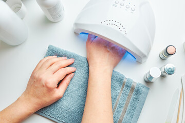 Woman preparing nails to apply gel hybrid polish using UV lamp. Beauty wellness spa treatment...