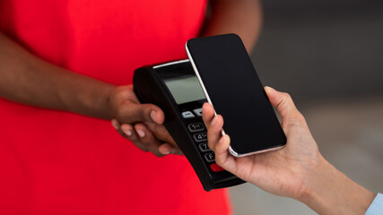 Black delivery man in uniform holding POS machine for payment