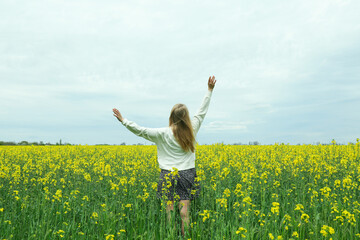 Naklejka na ściany i meble A girl stands in a rapeseed field on a summer day