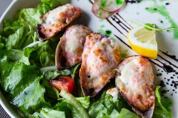 Top view mussels baked with cheese and cream sauce of seafood and red caviar, on a white plate with vegetables. High restaurant cuisine.