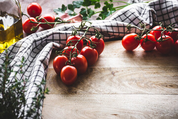 tomates cherry en rama sobre una tabla de cortar de madera, con aceite de oliva y hierbas...