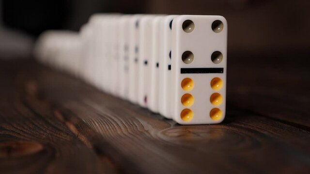 Hand of pushing dominoes on wooden background. A blurry image of domino bones, the first figure in sharpness. Domino Effect Concept.