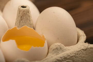 White chicken eggs and one broken egg in a tray made of white cardboard, close-up selective focus.