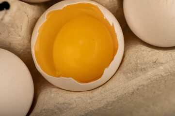 White chicken eggs and one broken egg in a tray made of white cardboard, close-up selective focus.