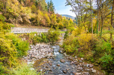 Magnificent landscape of a mountain river between large stones, an autumn forest, a highway and mountains