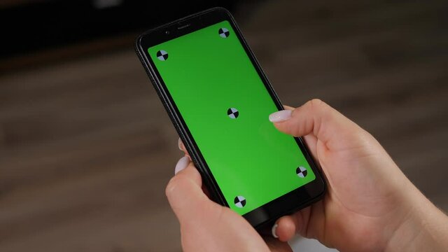 Close-up of woman's hand browsing smartphone with green screen at home. Woman at home relaxing reading on the smartphone with pre-keyed green screen.