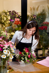 Florist works with colors. Flower in apron seller chooses flowers for future bouquet, concentrated. Flowers shop worker in flower shop, decorating and arranging different unusual blooming flowers