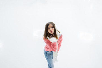 high angle view of young woman in ear muffs and scarf sending air kiss while skating on ice rink.