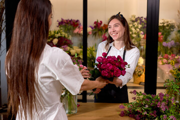 Nice caucasian woman florist giving beautifully decorated bouquet of pink roses for client,...