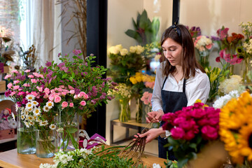 Young Female professional florist prepares the arrangement of wild flowers. Attractive caucasian lady in apron making bouquet. Flower shop. inspiration, floral, greetings, spring, ornament flowers